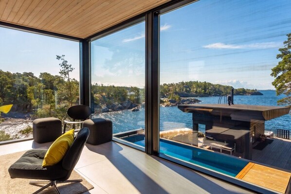 Una habitación moderna con un ventanal grande que da a una piscina y una vista panorámica de la costa rocosa.
