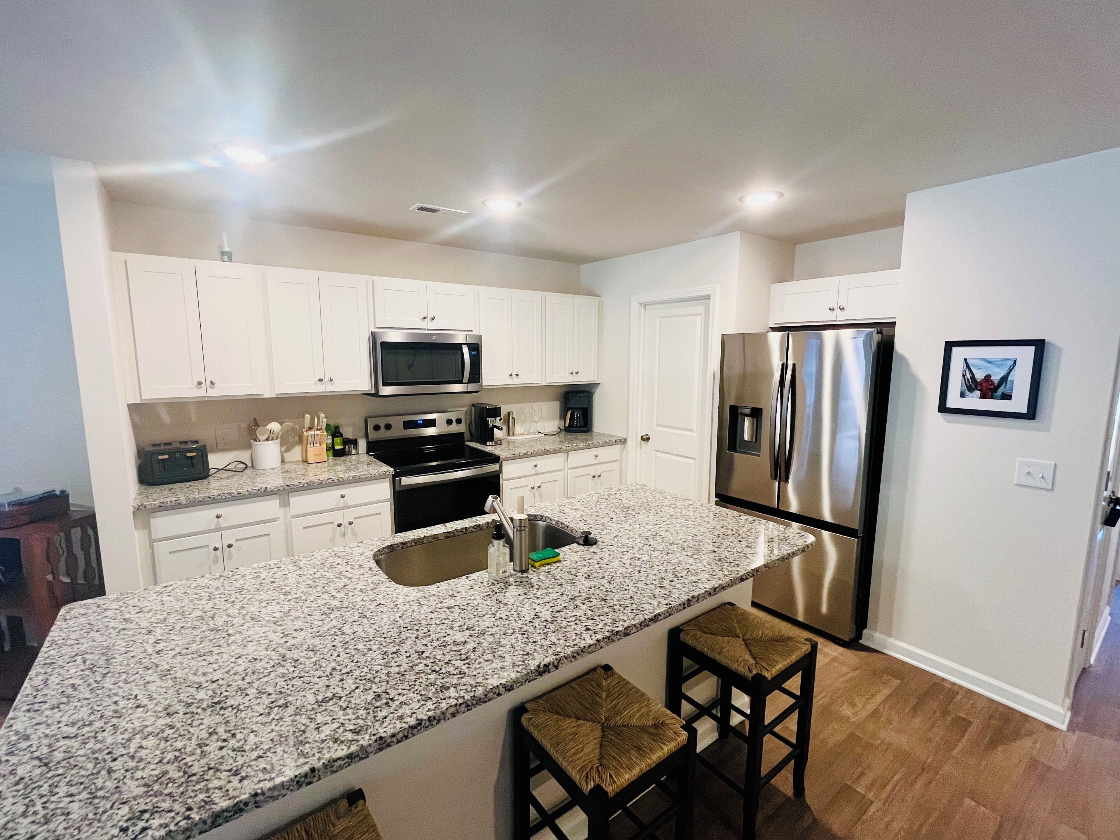 A modern kitchen with white cabinets, stainless steel appliances, granite countertops, and a bar area with stools.