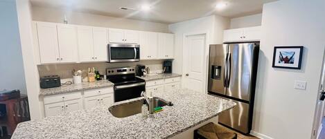 A modern kitchen with white cabinets, stainless steel appliances, granite countertops, and a bar area with stools.