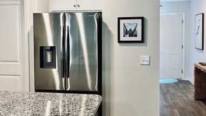 A modern kitchen with a stainless steel refrigerator, granite countertop, and wooden flooring. - Brand New Home with Open Floor Plan and Large Back Yard (Southport)