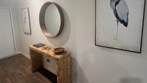 A hallway with a wooden console table, a round mirror, and a framed bird painting on the wall. - Brand New Home with Open Floor Plan and Large Back Yard (Southport)