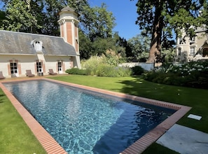 A swimming pool with a brick border, a building with a tower, and a well-maintained lawn.