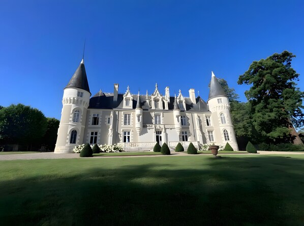 A large, historic building with multiple towers and a well-maintained lawn.