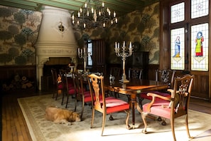 A dining room with a chandelier, wooden chairs, a fireplace, and a dog.