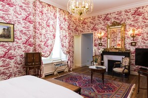 A room with floral wallpaper, a chandelier, a fireplace, a mirror, and a bed.