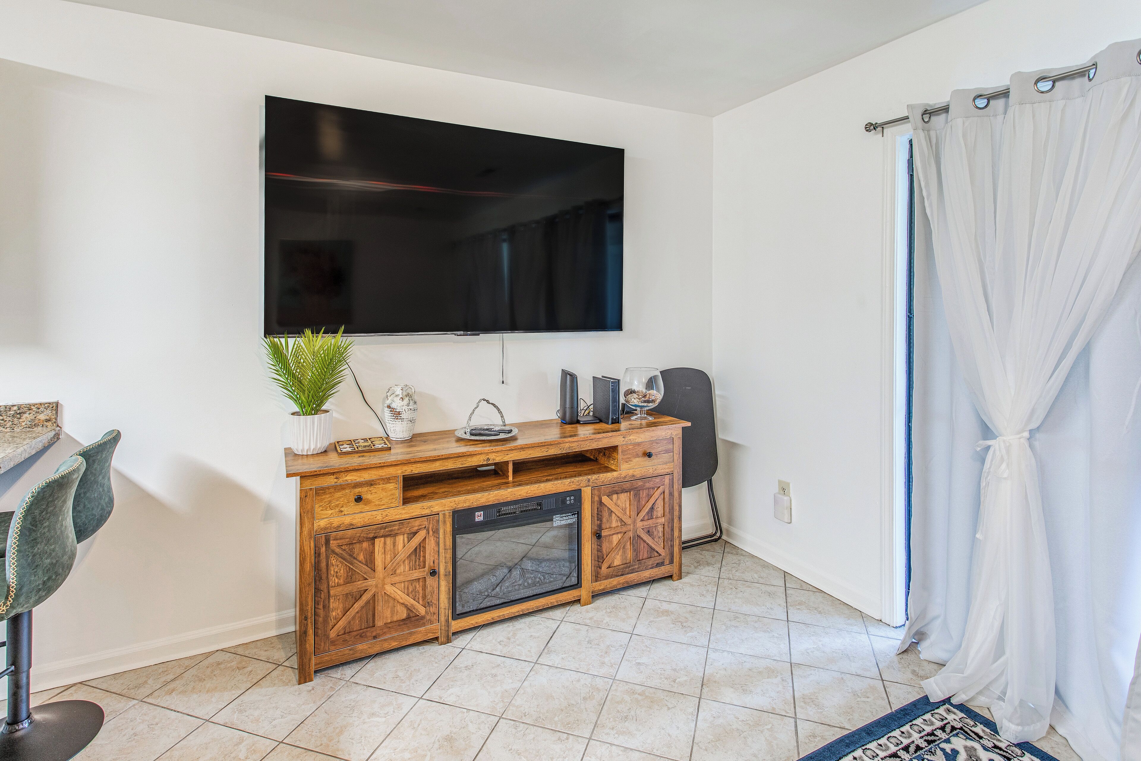 Un salon moderne avec un téléviseur à écran plat fixé au mur, un meuble de rangement en bois comprenant un lave-vaisselle, une plante en pot et une petite table agrémentée d’objets décoratifs.