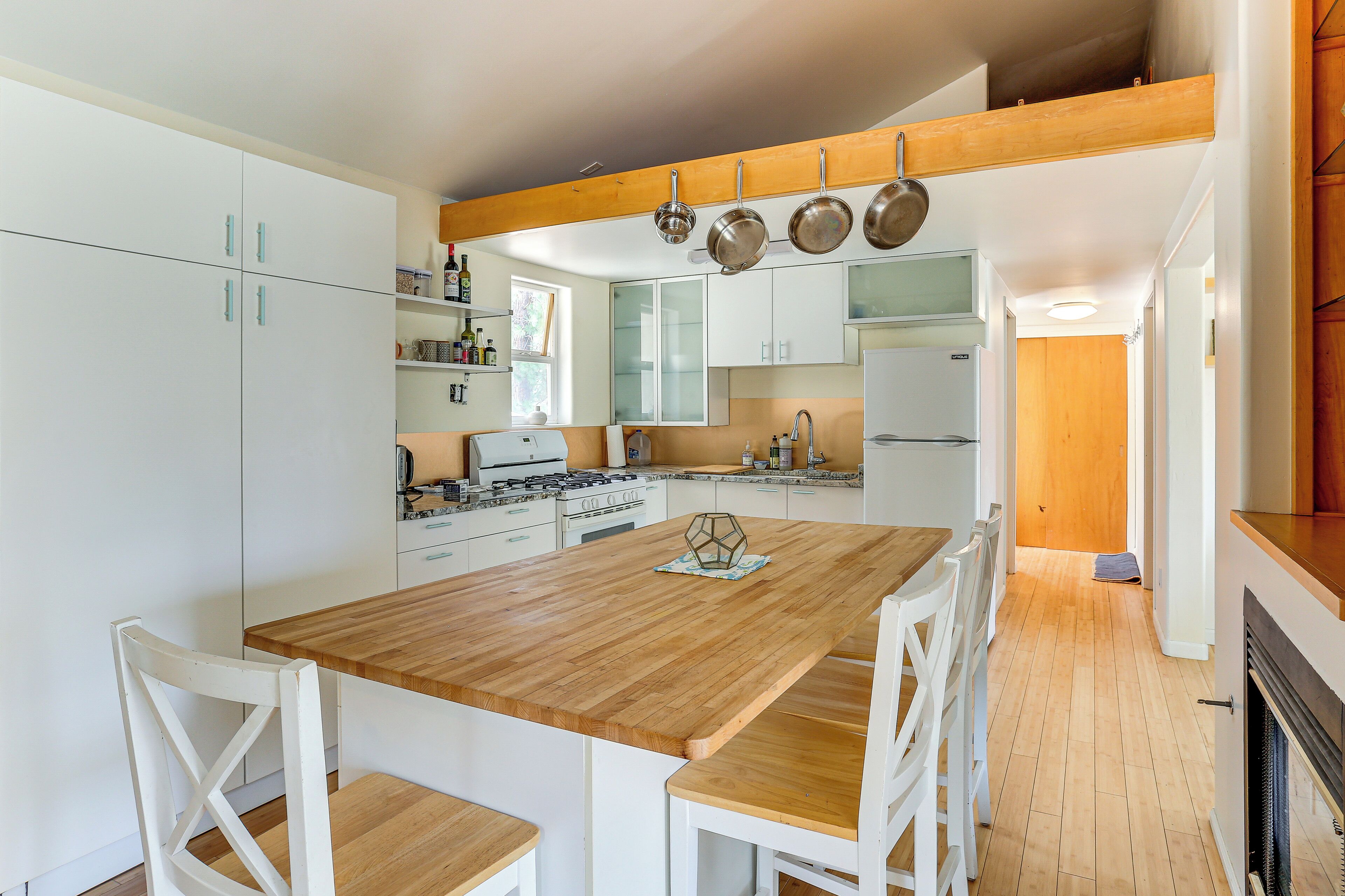 A modern kitchen with white cabinetry, a wooden dining table, and a built-in stove.