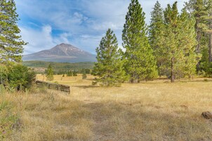 Un paisaje montañoso con cielo despejado, una valla de madera y varios árboles.