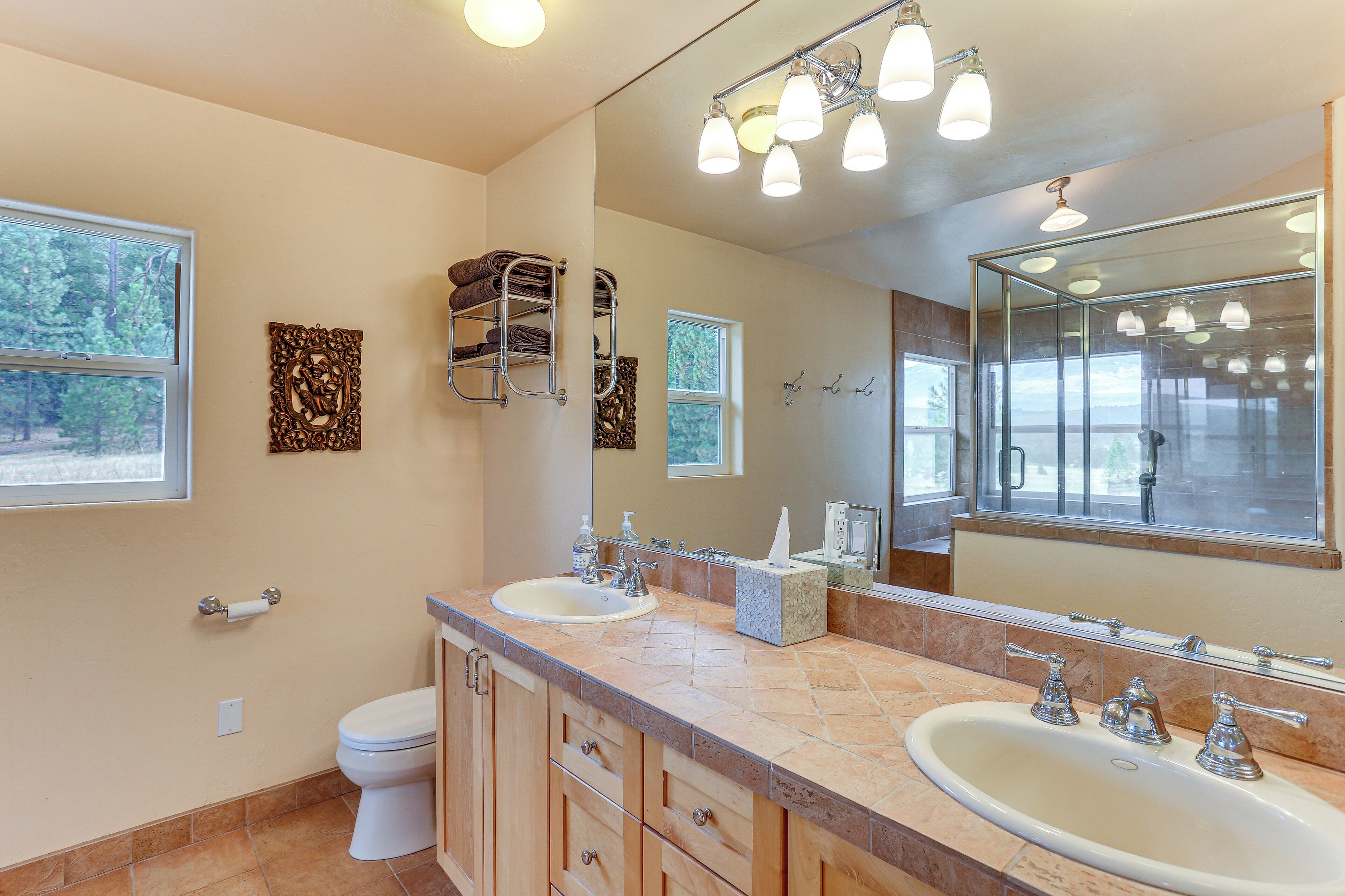 A bathroom with a double sink, a toilet, a towel rack, a mirror, and a window.