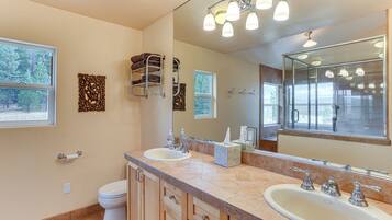 A bathroom with a double sink, a toilet, a towel rack, a mirror, and a window.