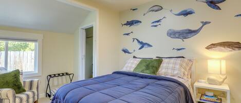 A bedroom with a large bed, a window, a chair, and a wall with whale decals.