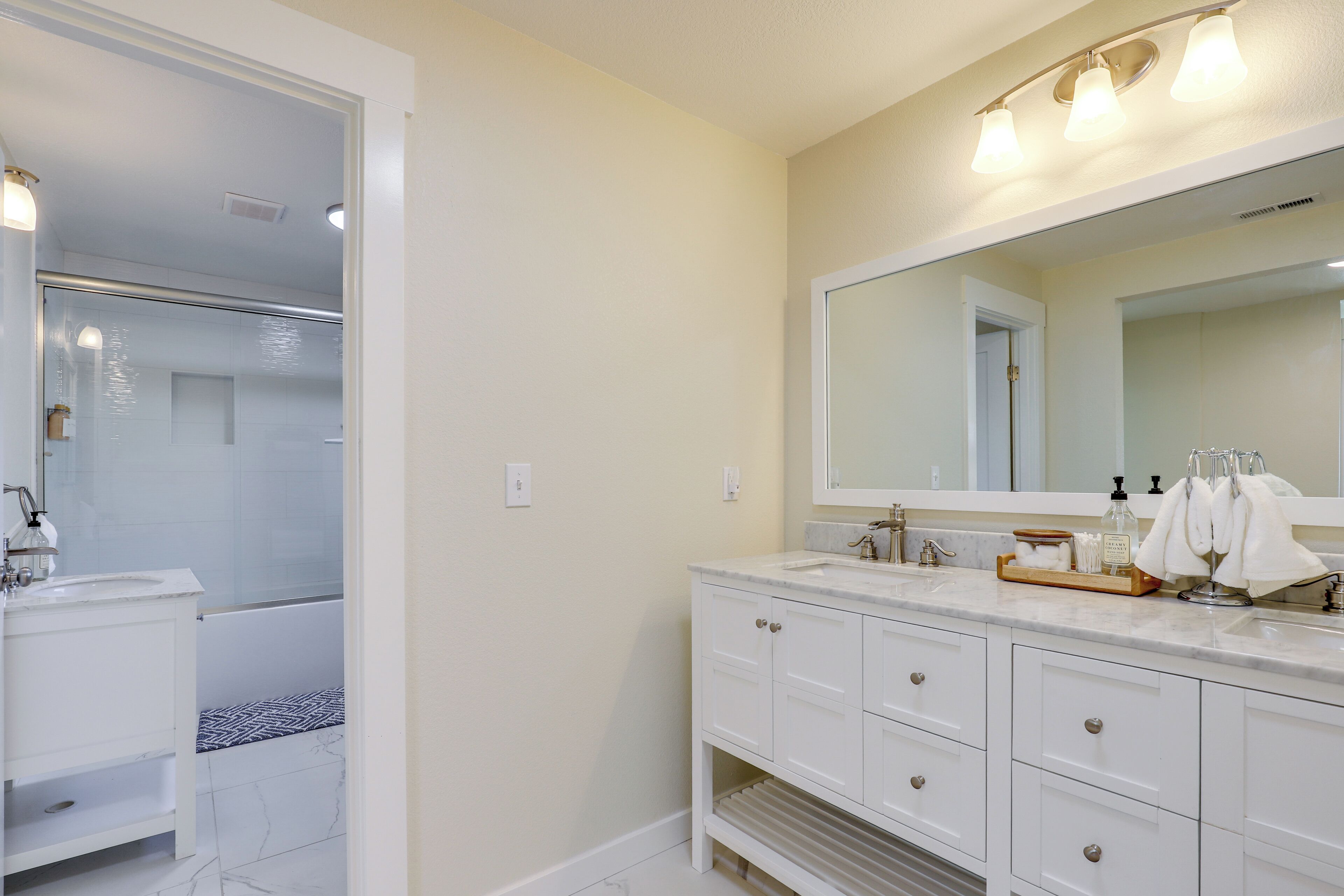 A modern bathroom with a large mirror, white vanity, and a shower area.