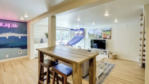 A spacious living area with a wooden table, a blue hammock, and a TV. - Walk to Dtwn Camas! Updated Home w/ Game Room (Camas)