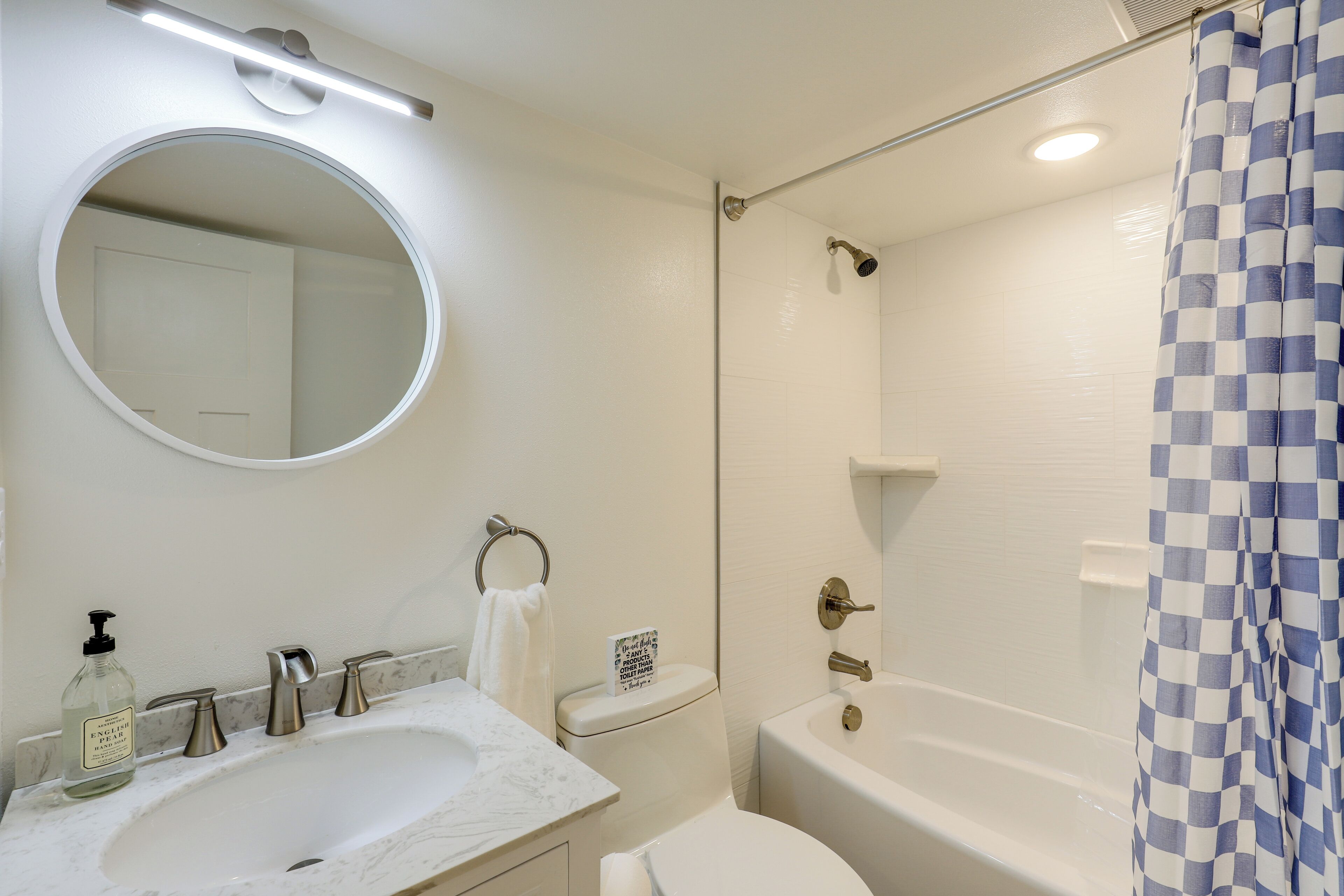 A bathroom with a round mirror, a sink, a toilet, and a bathtub.