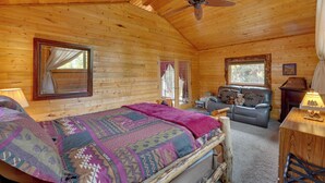 Une chambre située dans une cabane en rondins, avec un lit, un canapé, un bureau et un ventilateur de plafond.