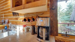 Une cuisine équipée d’une machine à café, d’un évier et d’une fenêtre donnant sur une forêt.