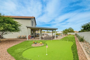 Un jardín trasero con un campo de práctica de golf, mobiliario de patio y una zona de estar cubierta.