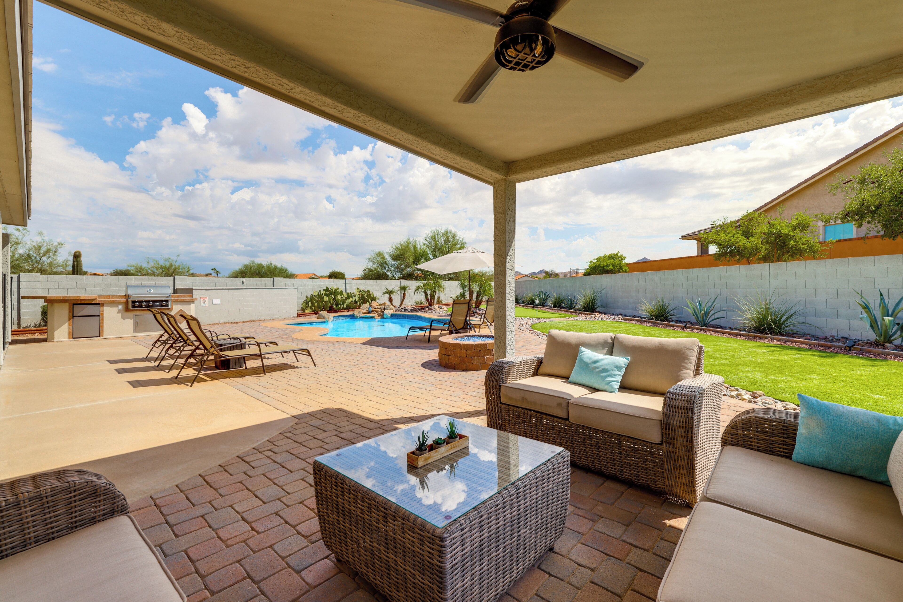 Um alpendre coberto com móveis de exterior, piscina e vista para o quintal.