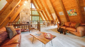 A spacious loft with a high ceiling, wooden beams, a stone wall, and a cozy seating area with leather sofas and a coffee table.