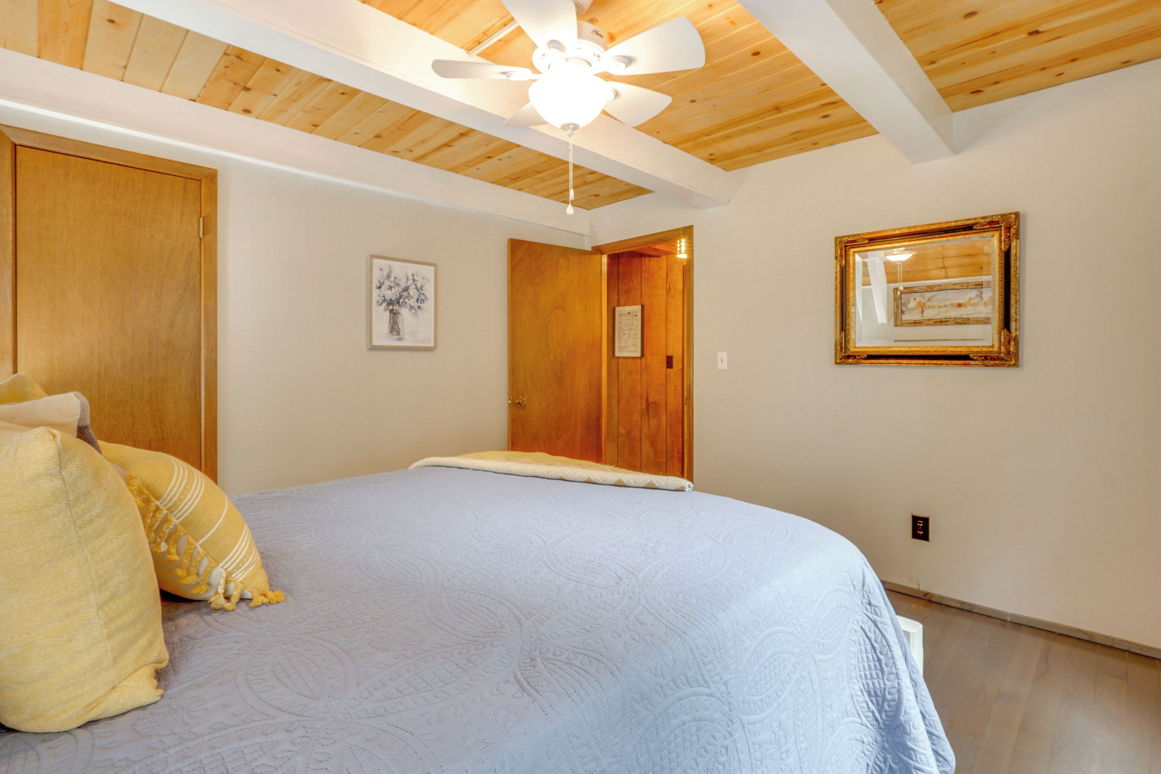A bedroom with a large bed, wooden ceiling, and a ceiling fan.