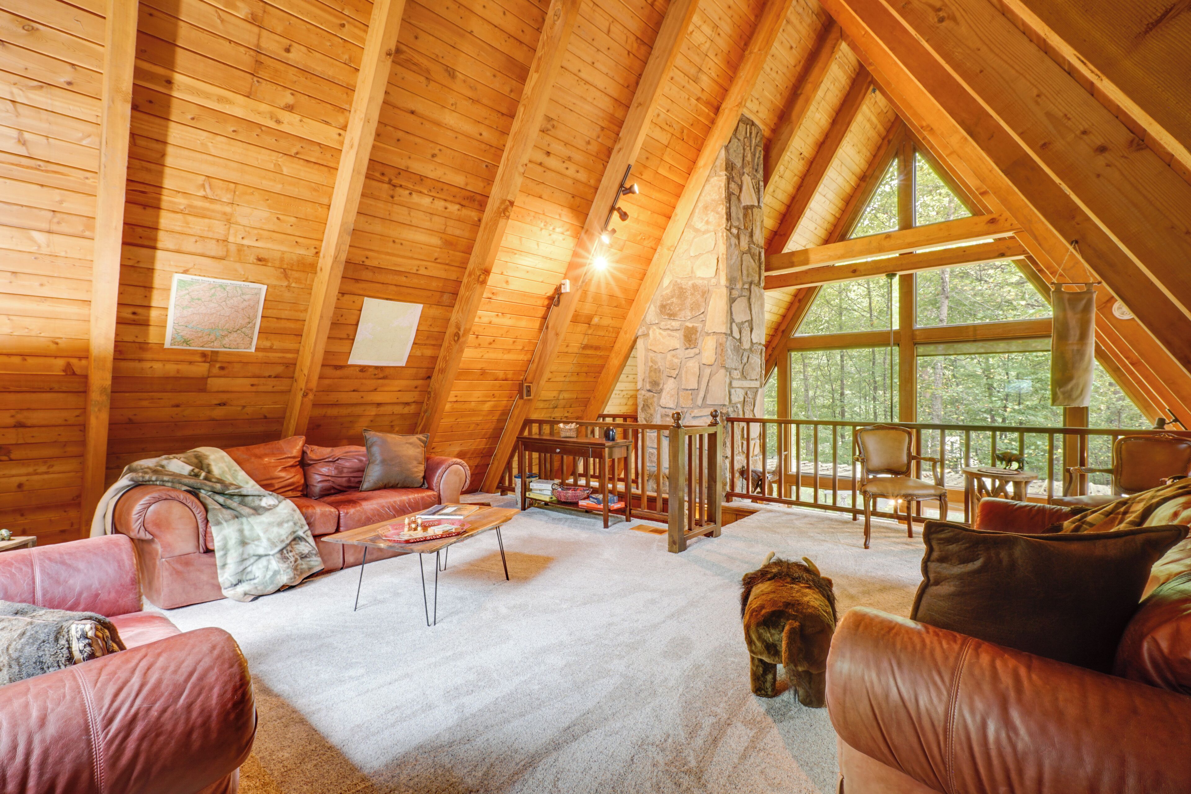 A cozy loft-style room with a high ceiling, wooden beams, a stone wall, and large windows offering a view of the outdoors.