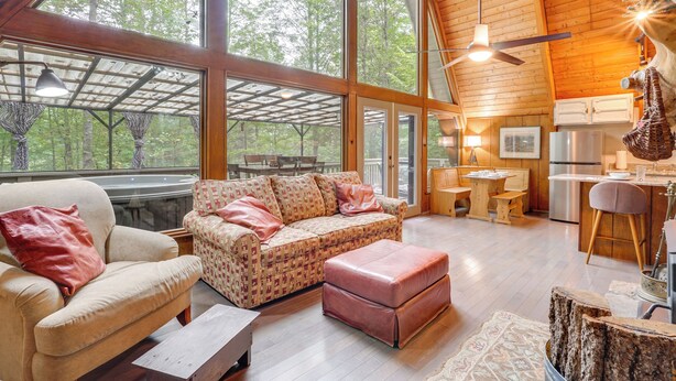 A spacious living area with a large window, a wooden ceiling, a sofa, a coffee table, and a kitchen area with a refrigerator and a sink.