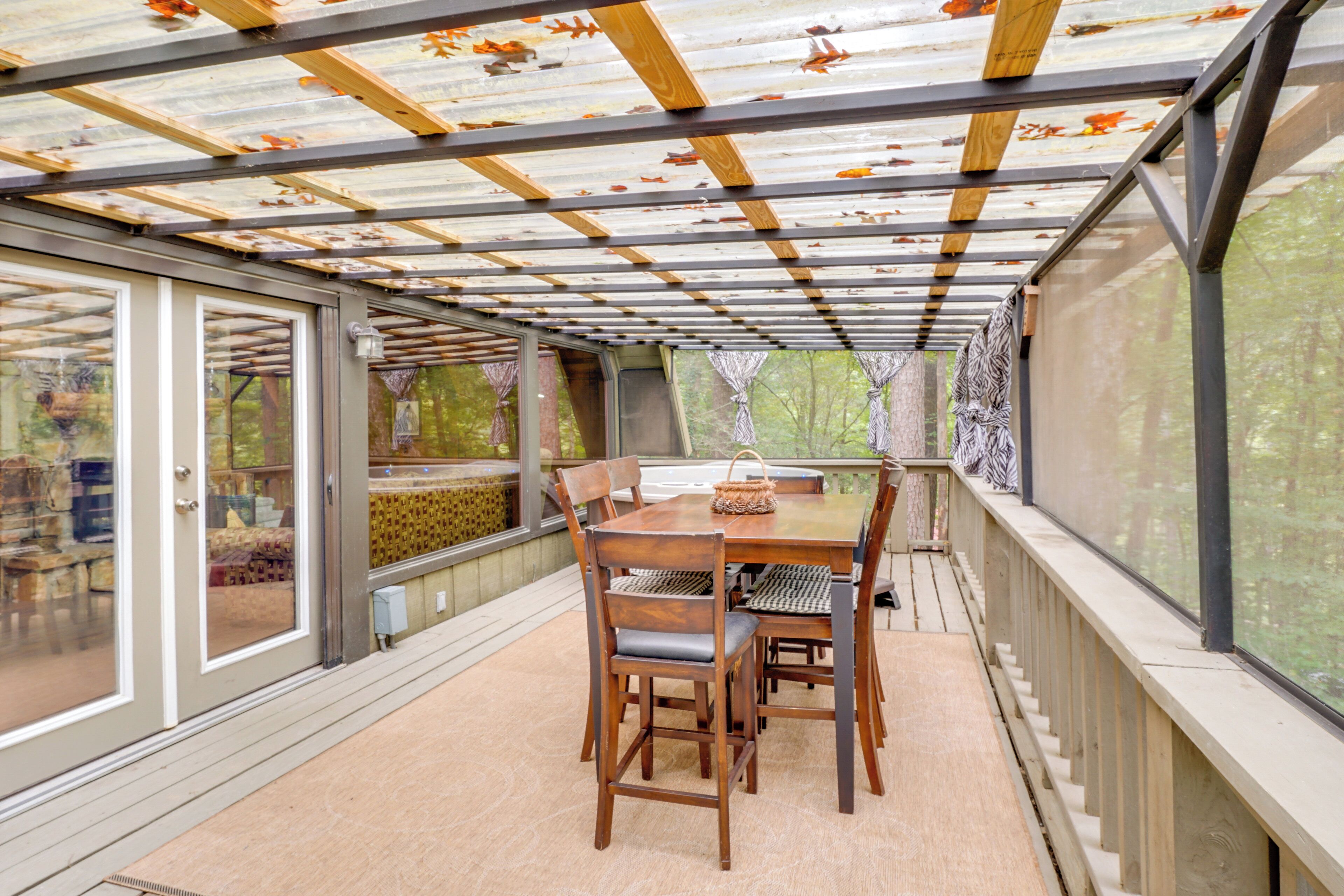 Un patio cubierto con una mesa y sillas de madera, ventanas amplias y una estructura de techo metálico.