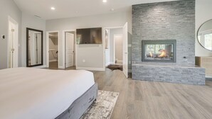 A modern bedroom with a large bed, a stone fireplace, and a view of the bathroom.