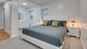 A modern bedroom with a large bed, bedside tables, a mirror, and a window.