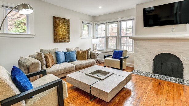 A living room with a sofa, armchairs, a coffee table, a fireplace, and a TV mounted on the wall.