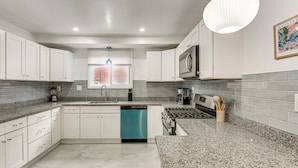 A modern kitchen with white cabinets, a teal dishwasher, granite countertops, a gas stove, and a hanging light fixture.