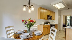 A dining area with a wooden table set for four, surrounded by white chairs. A vase with flowers is on the table. - Bike & Explore: Family Home in The Woodlands! (The Woodlands)