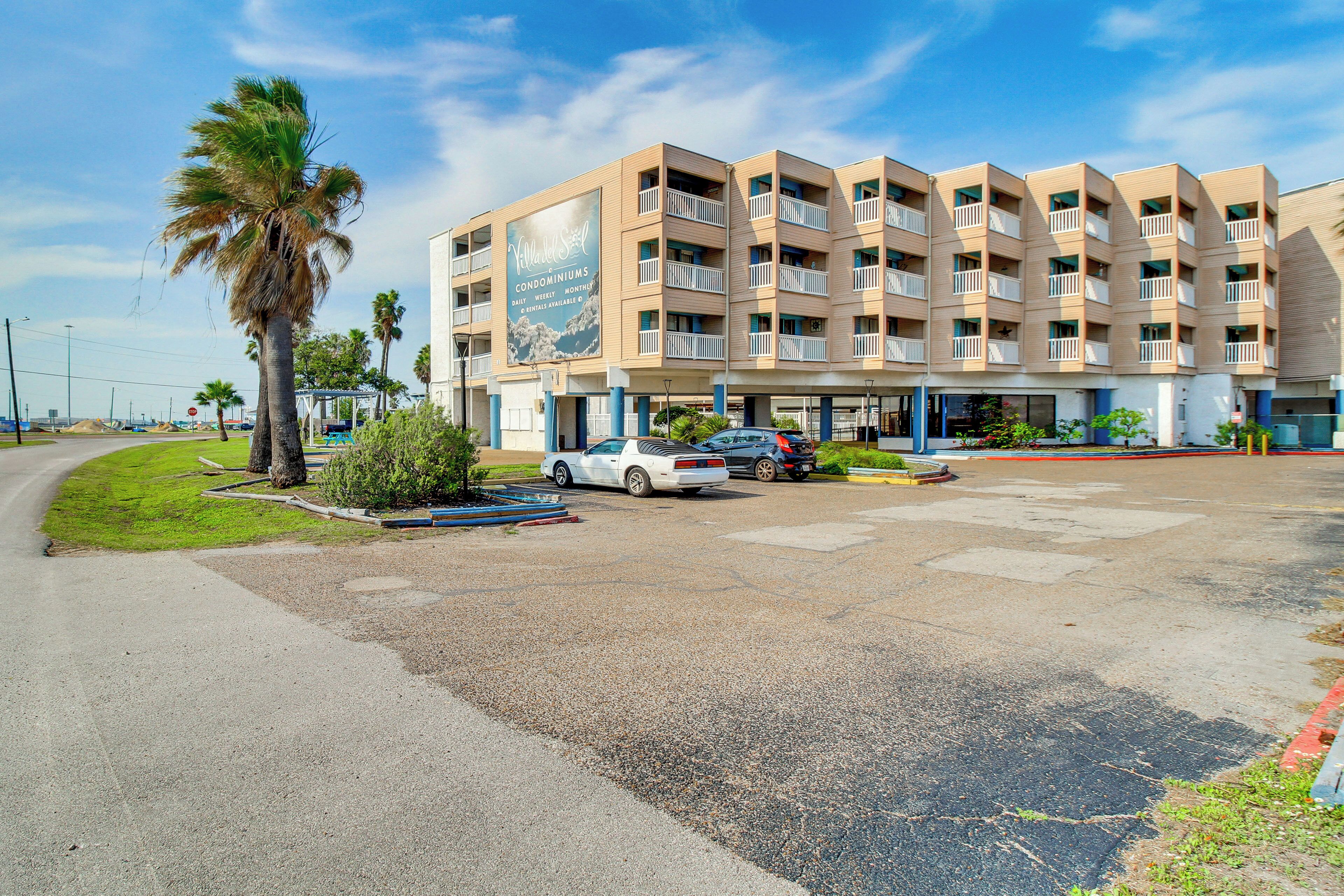 A multi-story hotel with balconies, a parking lot, and a palm tree.