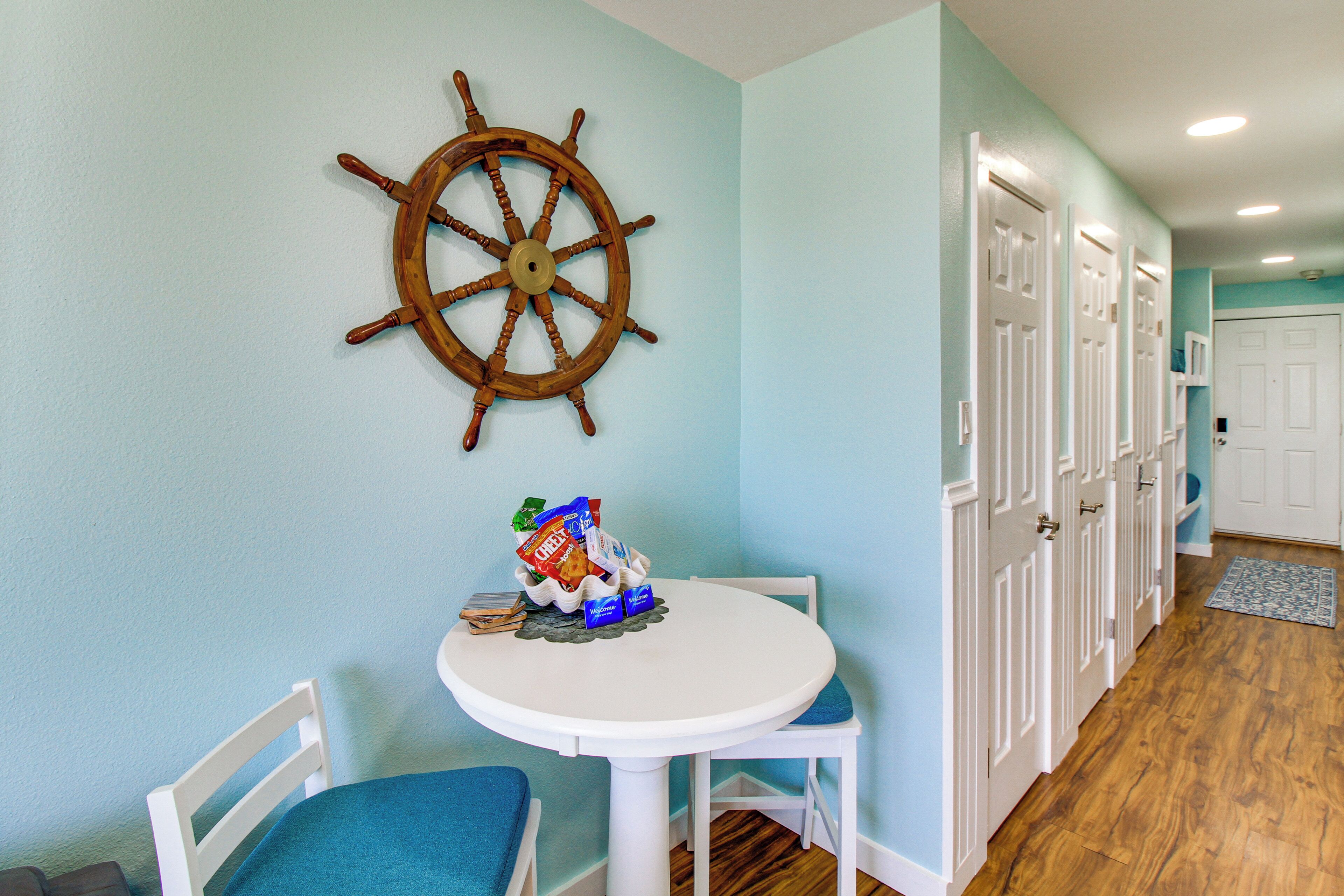 A dining area with a white table and chairs, a ship's wheel decoration, and a hallway with white doors.
