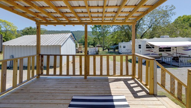 A wooden deck with a metal roof, overlooking a campsite with RVs and a small building.