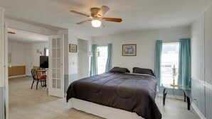 A bedroom with a bed, a ceiling fan, a desk with a chair, and a window with curtains.