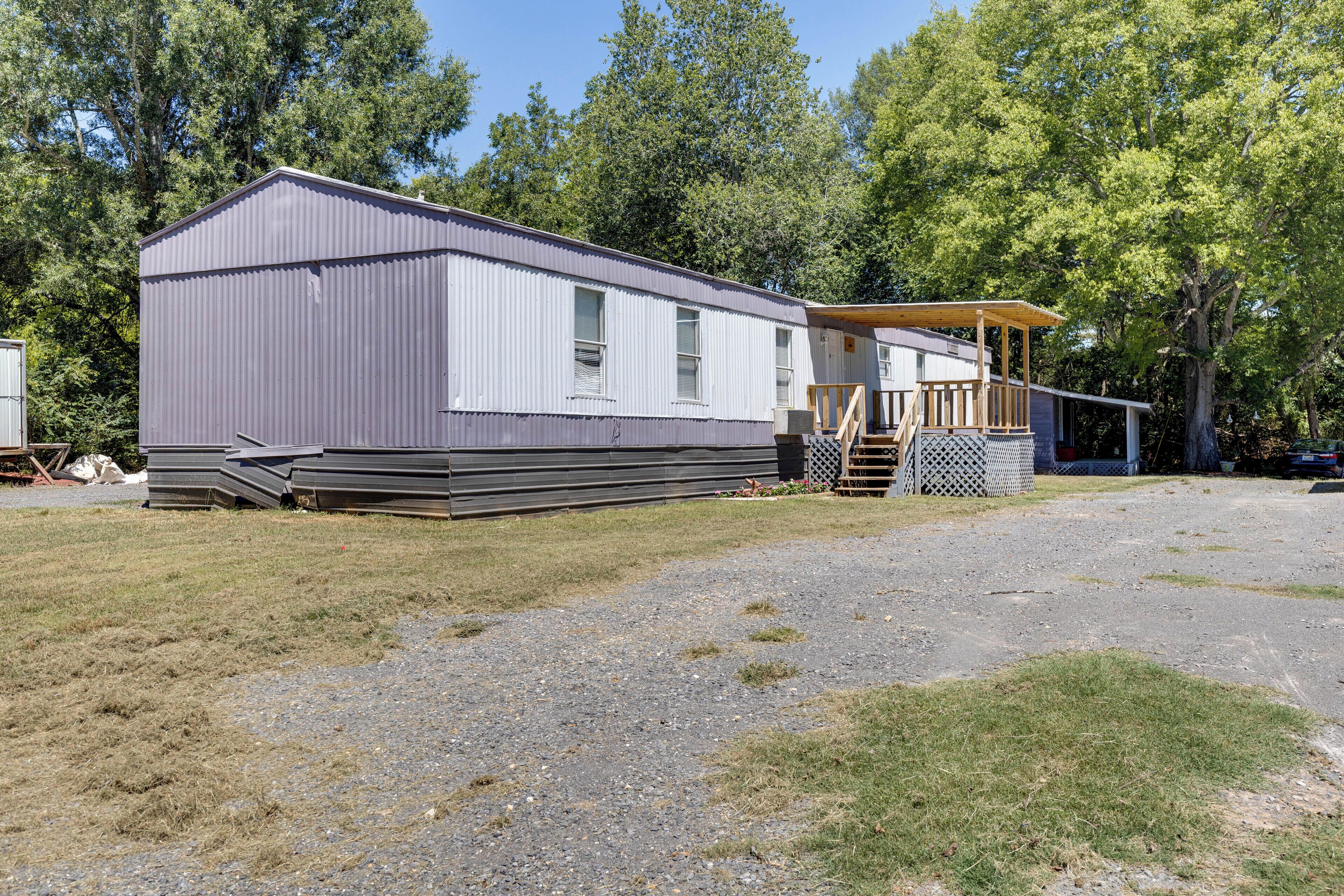 A mobile home with a covered porch and a small deck, surrounded by trees.