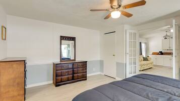 A bedroom with a bed, a dresser, a ceiling fan, and a door leading to a living area.