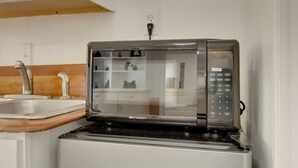 A compact microwave oven with a digital control panel, positioned on a white countertop next to a stainless steel sink.