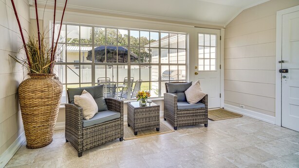 A sunroom with wicker furniture, a large vase with flowers, and a view of the outside.