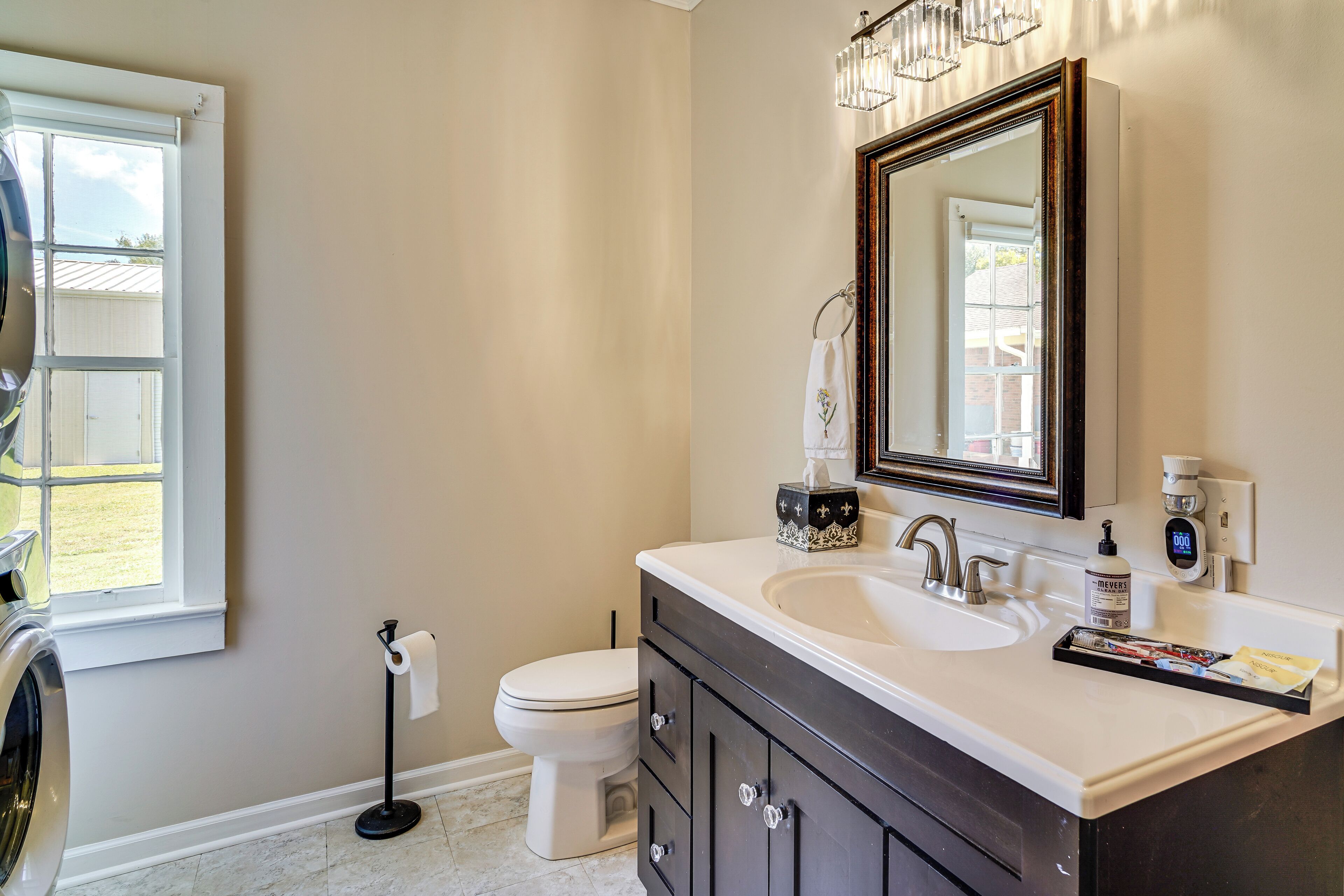 A bathroom with a large window, a toilet, a sink, and a mirror.
