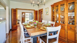 A dining room with a wooden table set for six, surrounded by white chairs, and a wooden cabinet with glass doors on the right.