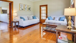 A living room with two white sofas, wooden flooring, a coffee table, and a door with a window.