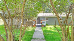 A pathway leading to a house with a front porch, surrounded by trees and a grassy yard.