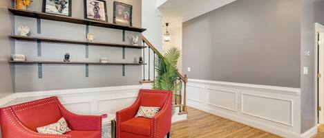 A living room with a red armchair, a matching armchair, a wooden floor, a white wall, and a staircase.