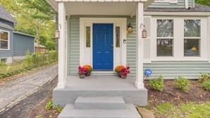 Una casa con puerta azul, porche blanco y dos macetas en los escalones.