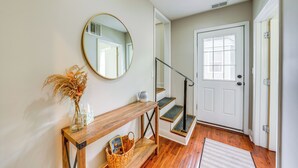 Un couloir avec une console en bois, un miroir, un vase contenant des plantes séchées, un panier et un escalier menant à une porte dotée d’une fenêtre.