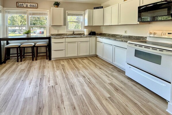 A kitchen with white cabinets, a wooden floor, a built-in island with stools, a stove, and a microwave. - Half-mi to Dtwn Yankton & River: Charming Home! (Yankton)