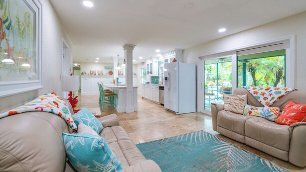 A spacious living area with a beige sofa, a dining table, and a kitchen in the background. - Outdoor Oasis w/ Bar & Lanai: Tavares Escape (Tavares)