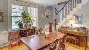 A dining room with a wooden table, chairs, a piano, and a staircase.